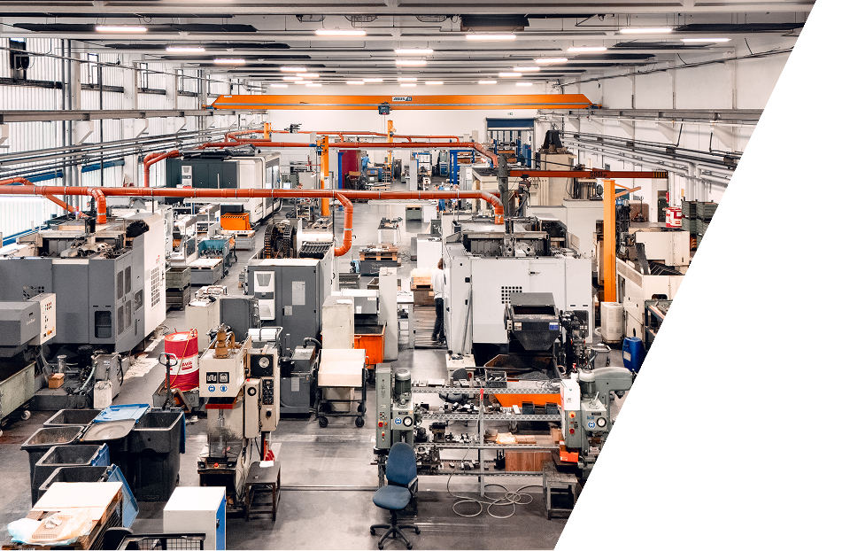 Ein großes, modernes Fabrikgebäude voller industrieller Maschinen, Arbeitsplätze und Geräte. An der Decke sind orangefarbene Kräne angebracht, und in dem sauberen, organisierten Raum sind verschiedene Werkzeuge und Wagen verteilt.