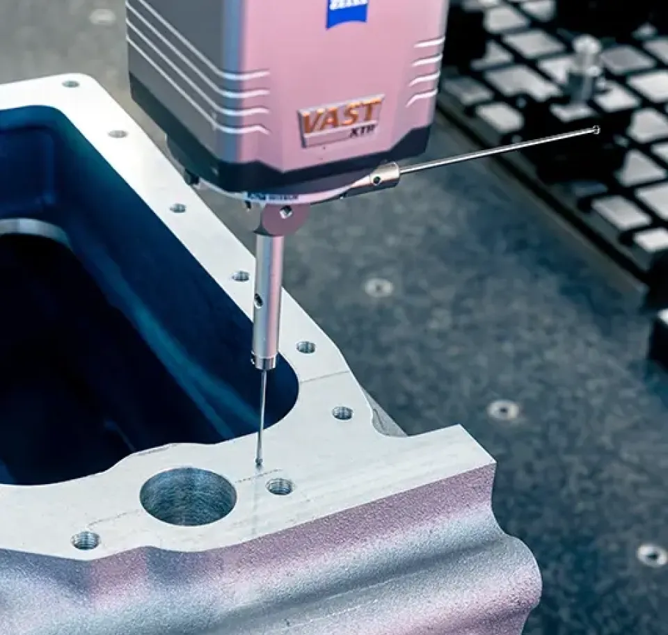 Ein Tastkopf eines Koordinatenmessgeräts (KMG) prüft ein Motorbauteil aus Metall für präzise Messungen in einem Qualitätskontrollverfahren.